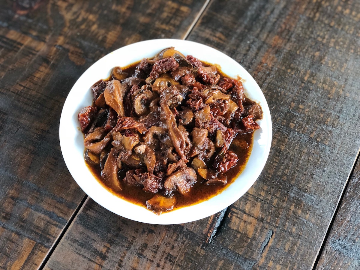 Smokey mushrooms with sundried tomatoes, vegan, plantbased on white plate on wooden, dark brown background