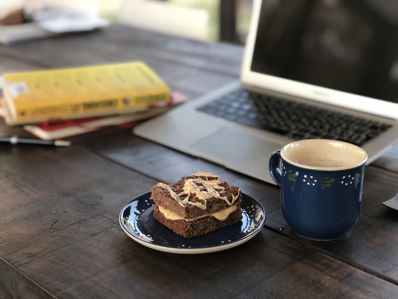 Banana-Bread-Squares on blue plate with coffee and laptop and book on wooden table