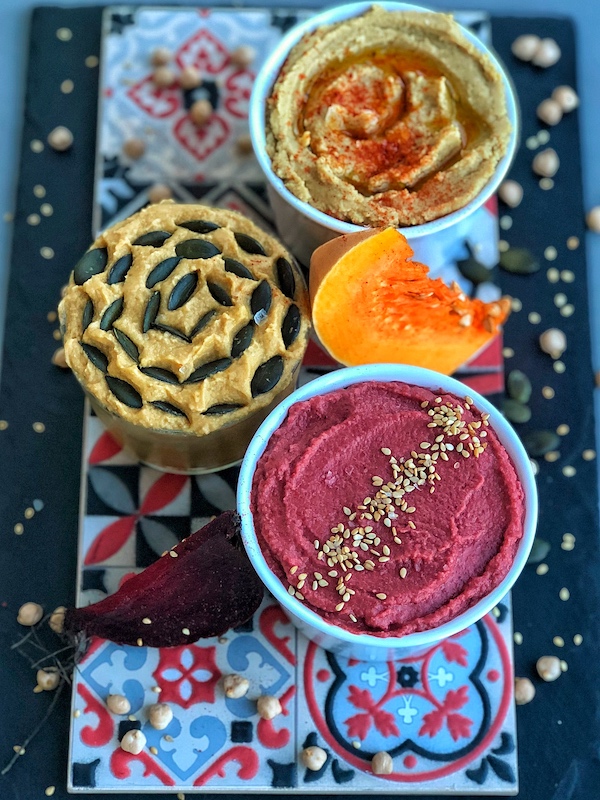 3 different hummus on one ceramic plate, beet, pumpkin and classic hummus
