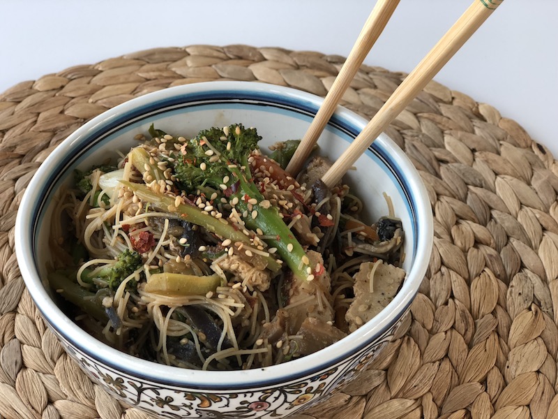 Fideos de arroz con espinaca y verduras en un bol con palillos chinos