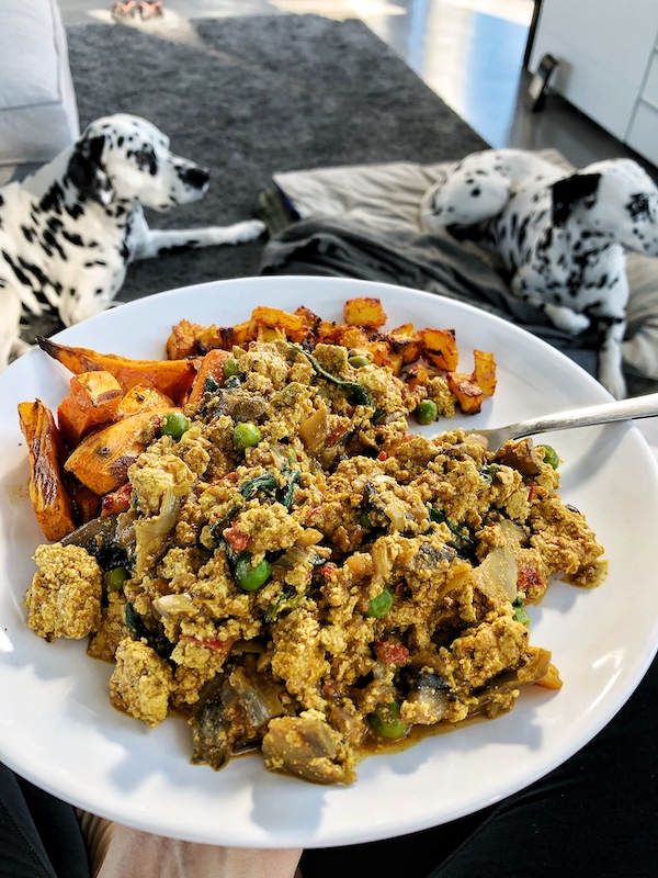 Scrambled tofu with veggies on a white plate with baked potato cubes