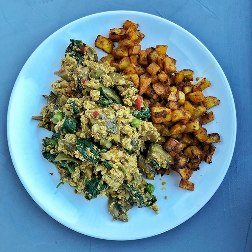 Scrambled tofu with veggies on a white plate with baked potato cubes
