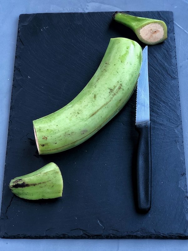Plátanos verdes (macho) encima de pizarra negra con cuchillo